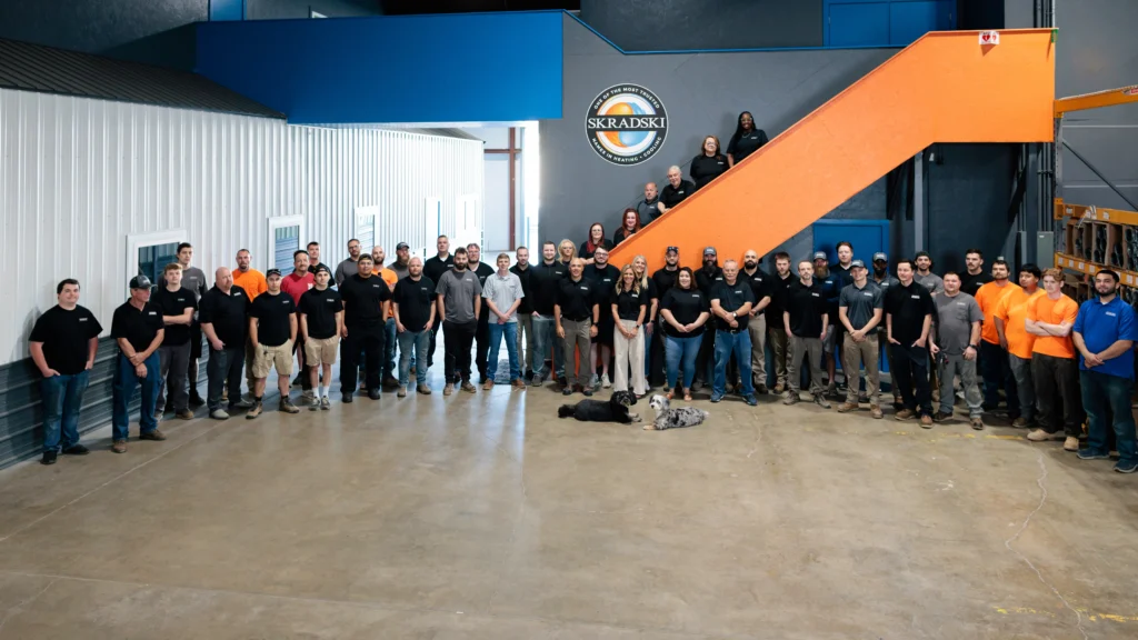 A large group of people pose for a photo inside a spacious industrial building, some standing on the ground and others on an orange staircase.